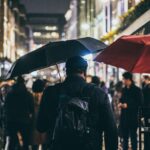 Man carrying a black EDC umbrella through a busy, rain-soaked city street at night.