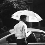 A man in business attire holding an ultra compact umbrella in the rain while opening his car door, highlighting the practicality and portability of ultra compact umbrellas for everyday carry