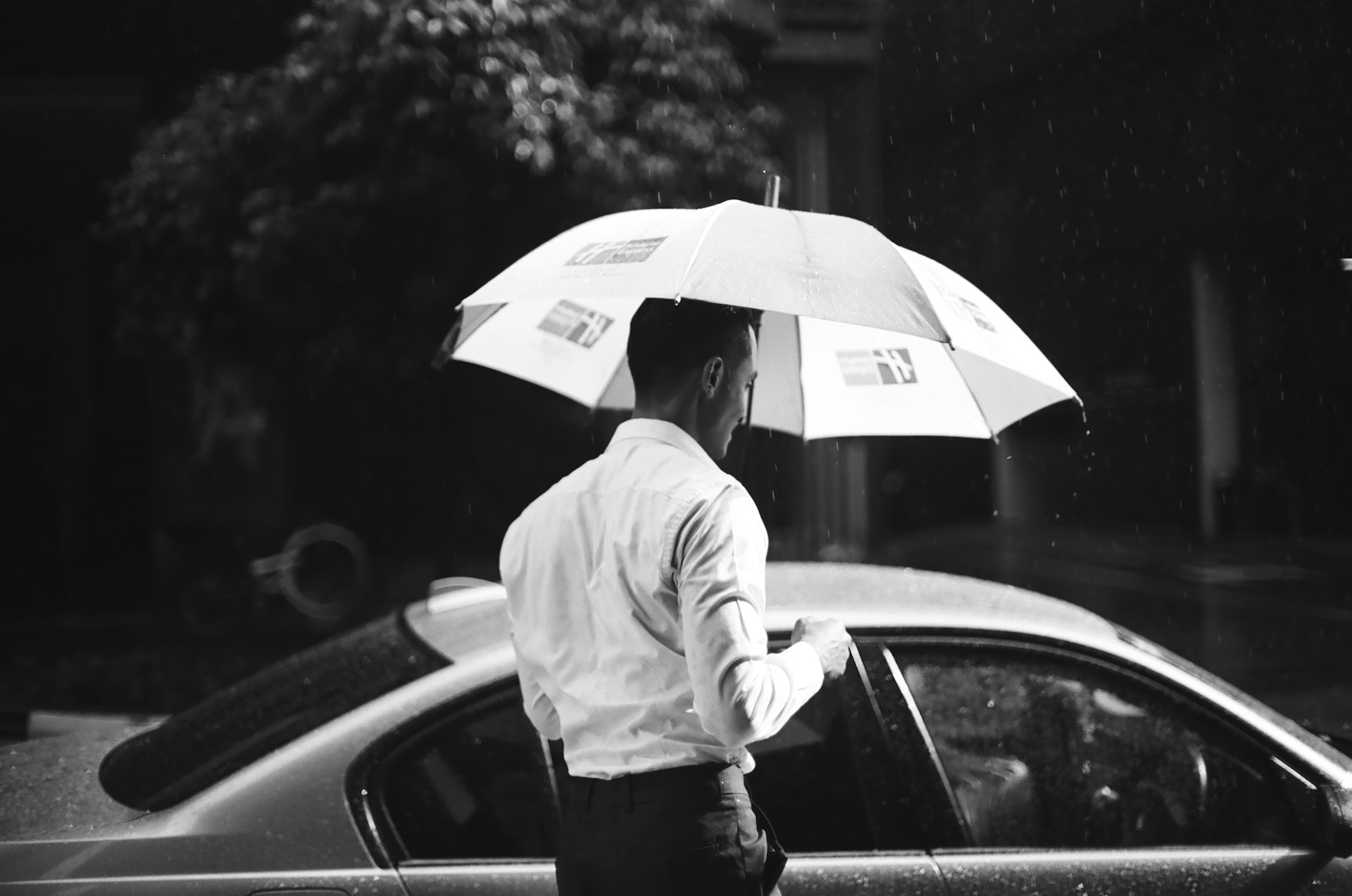 A man in business attire holding an ultra compact umbrella in the rain while opening his car door, highlighting the practicality and portability of ultra compact umbrellas for everyday carry